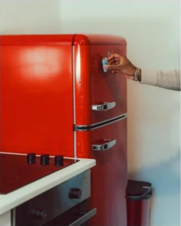 Hand reaching for the handle of a red retro-style refrigerator in a kitchen