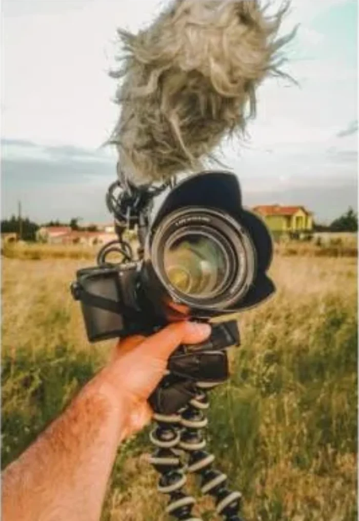 Content creator holding a camera with microphone outdoors in a field